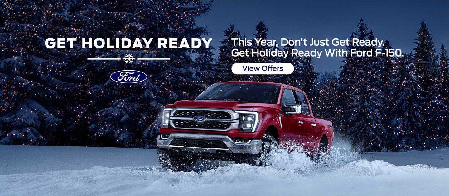 A 2021 Ford F-150 Being driven through deep snow at night, snow covered pine trees with Christmas lights on branches in background.
