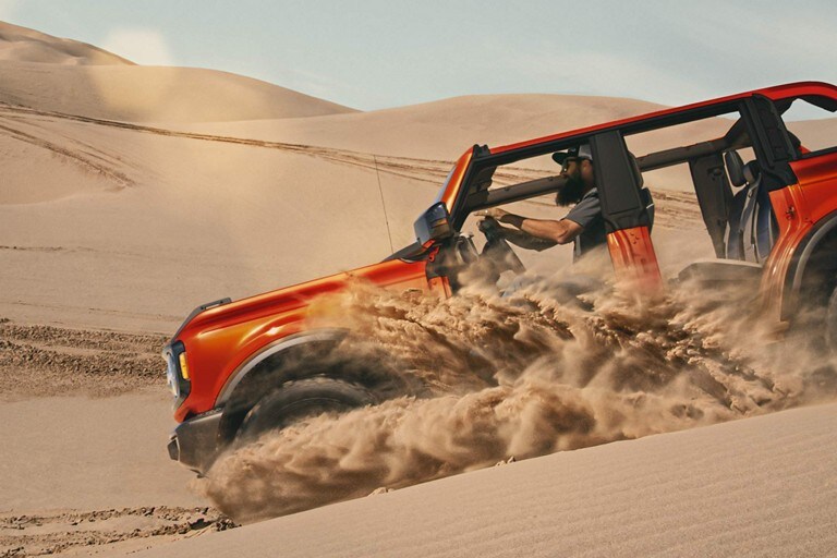 Modelo de una Ford Bronco® 2023 en Hot Pepper Red Metallic conduciendo por una duna de arena