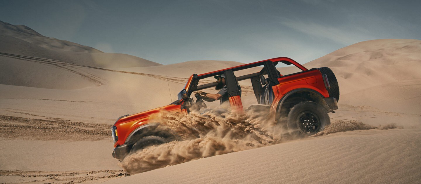 A four-door 2023 Ford Bronco® SUV being driven over sand dunes with the doors and top removed