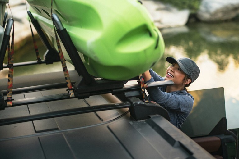 A woman placing a kayak in the rack atop her 2023 Ford Bronco®