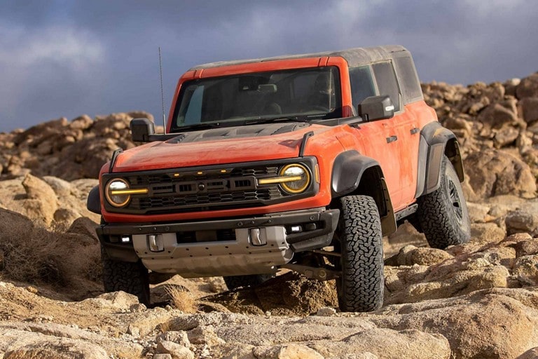 Una Ford Bronco® Raptor® 2023 de cuatro puertas en Hot Pepper Red (pintura con costo adicional) andando por las rocas
