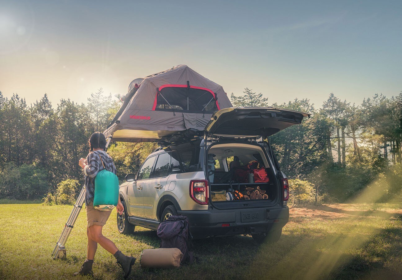 Se muestra una Ford Bronco® Sport 2023 con carpa en el techo y zona de carga trasera llena de cosas y una mujer parada fuera del vehículo