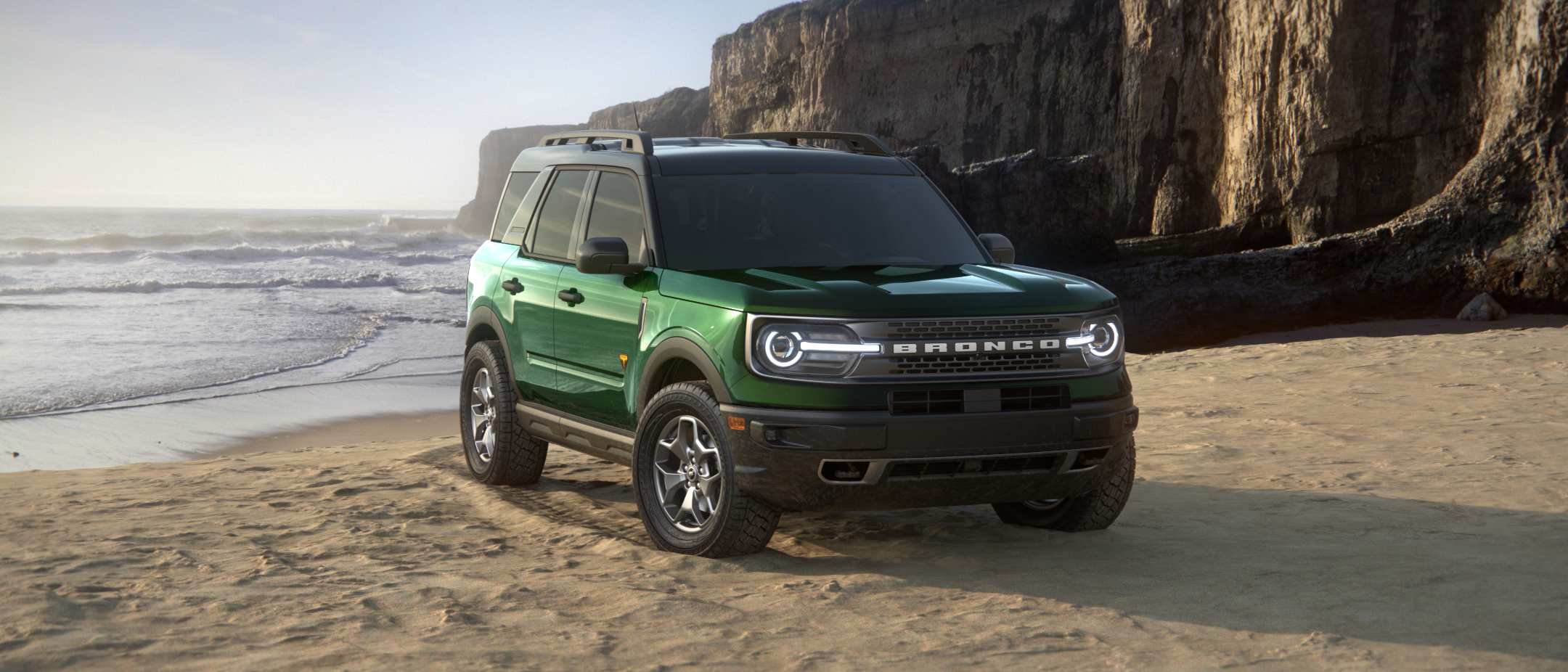 2023 Ford Bronco Sport in green, parked on a beach with the ocean and cliffs in the background