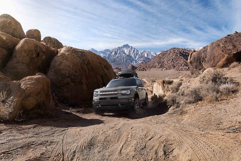 Una SUV Ford Bronco® Sport 2023 circulando por un camino de tierra con montañas a la distancia.