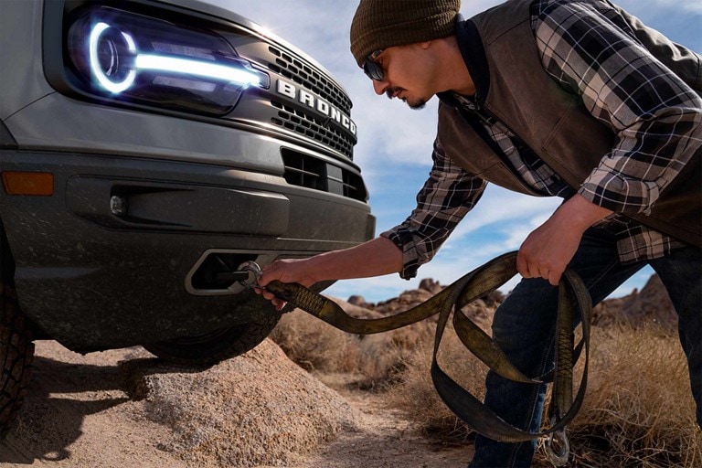 Un modelo Bronco® Sport 2023 con un hombre enganchando una correa en los ganchos para remolque delanteros