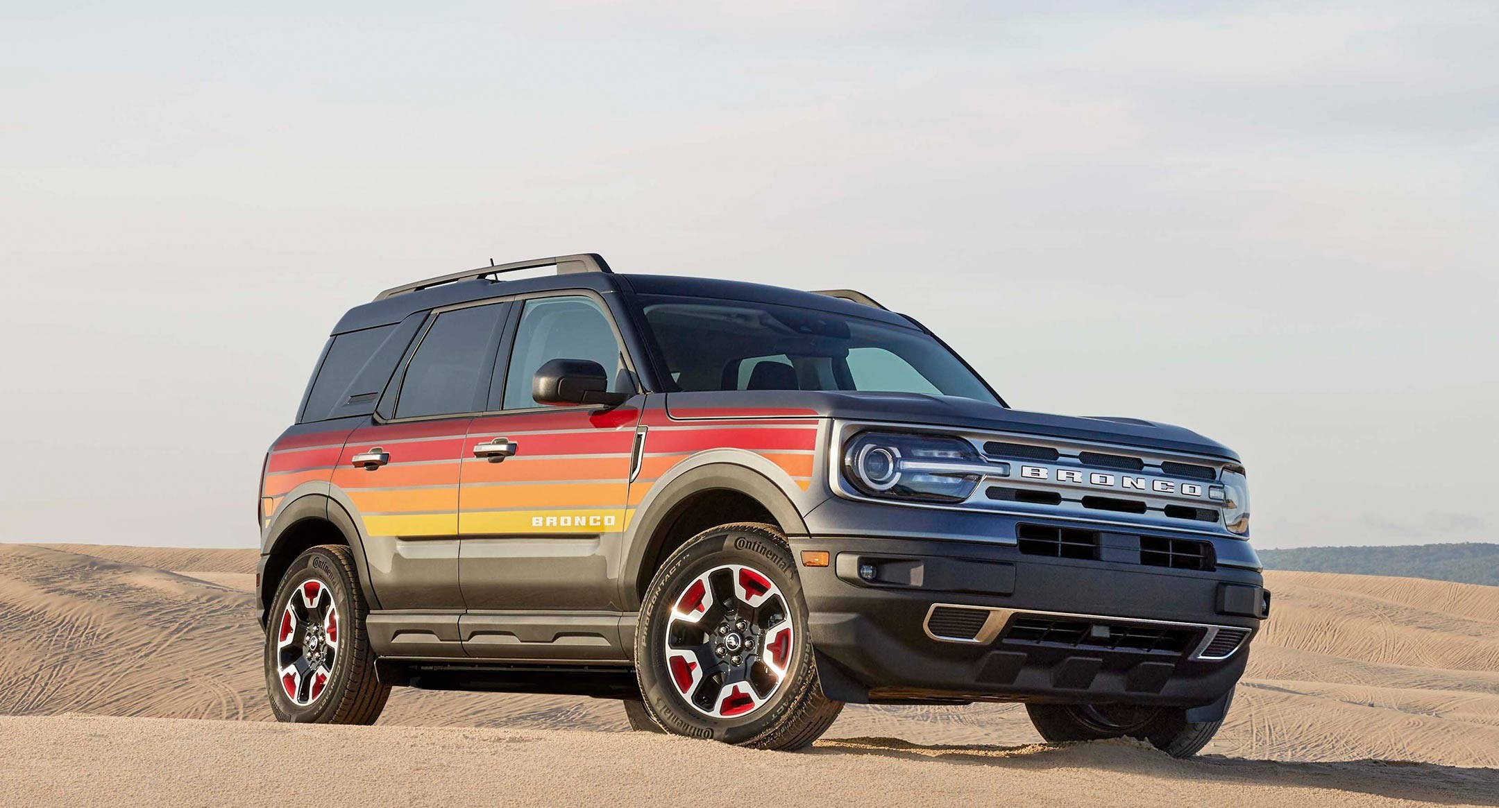 2024 Black ombre to gold painted Ford Bronco Sport with ombre red to yellow decals on side profiles parked in a sand dune