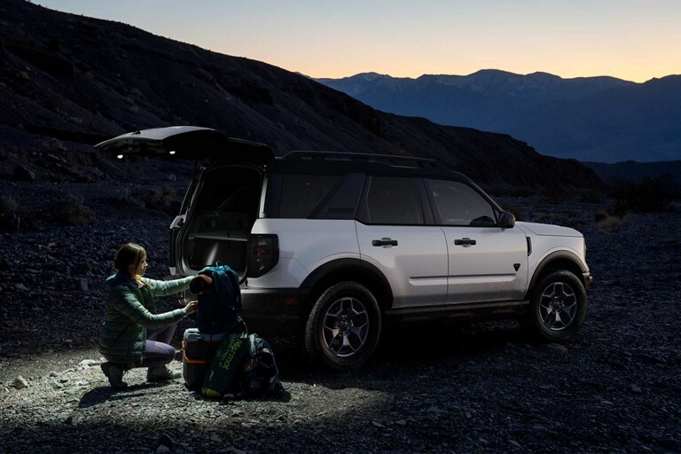 A person with camping gear near the open liftgate of a 2024 Ford Bronco® Sport model with rear floodlights illuminated