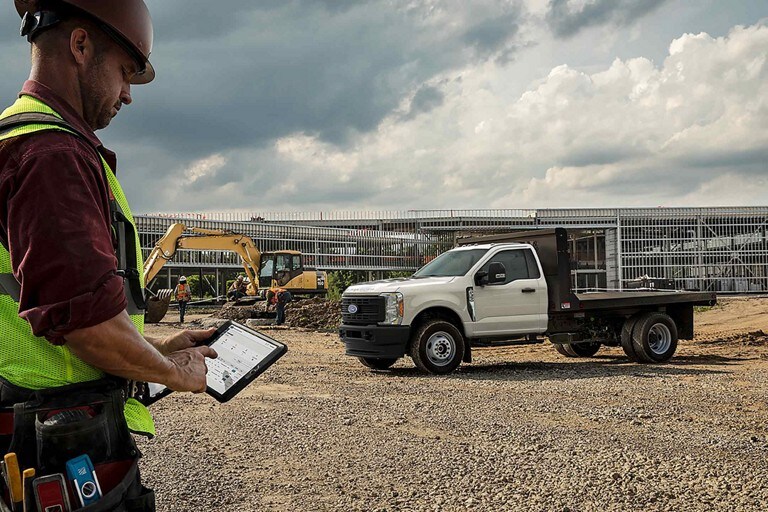 Worker using a tablet at construction site while a 2024 Ford Super Duty® Chassis Cab is parked in the background
