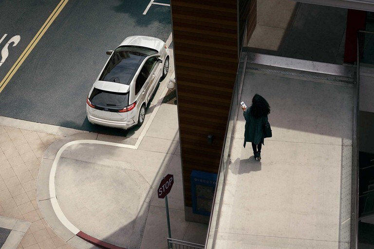Woman holds a smartphone on a walkway overlooking her 2024 Ford Edge® parked on the street below