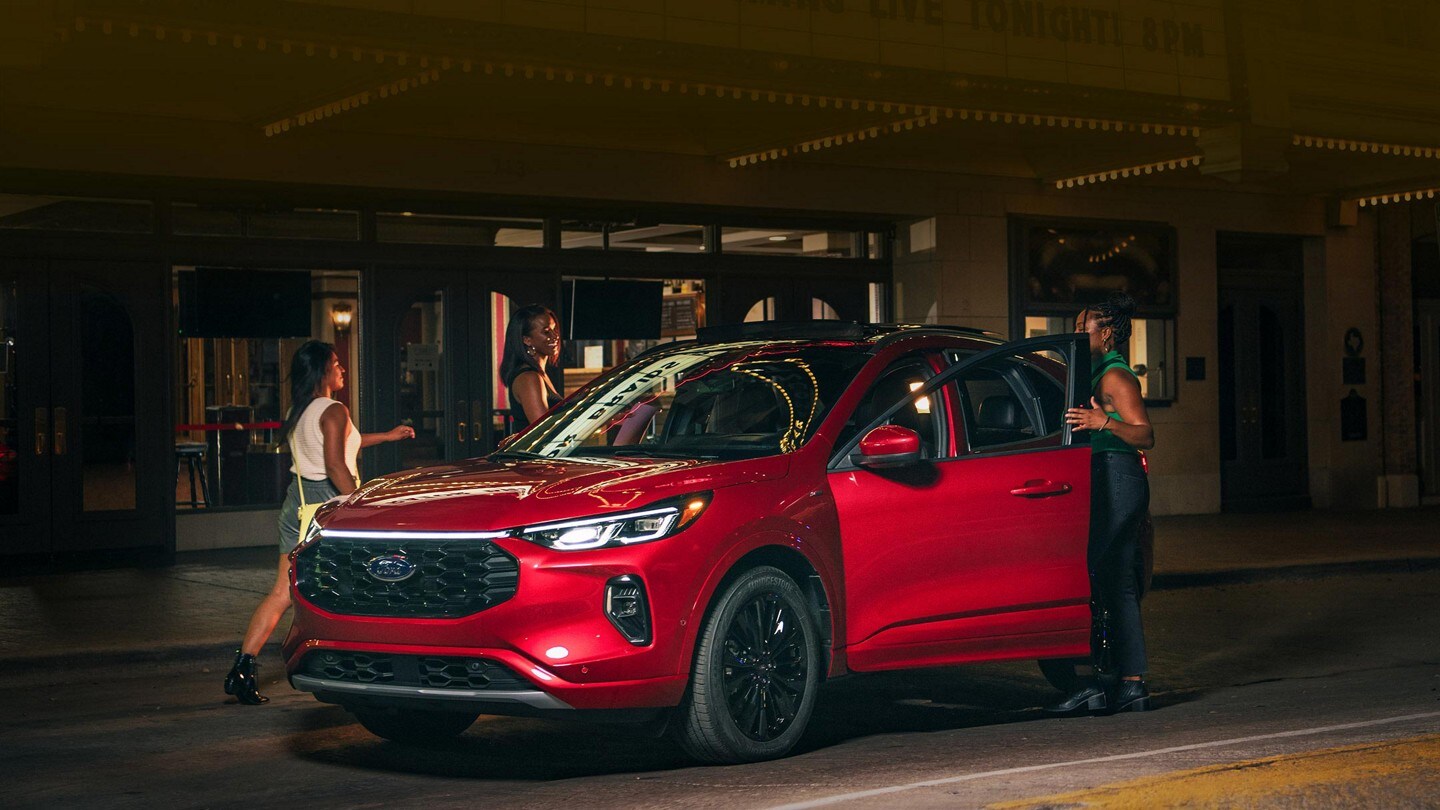 Una Ford Escape® 2023 estacionada de noche frente a un teatro y una mujer que entra