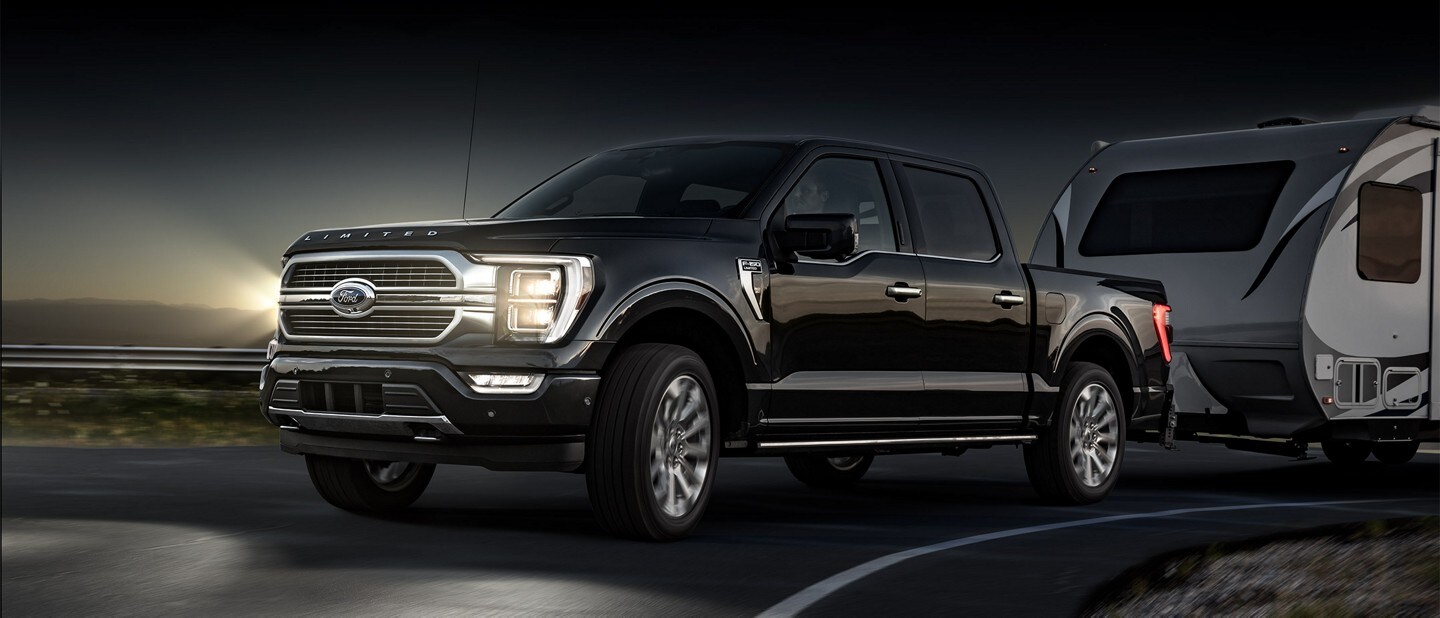 Una Ford F-150® 2023 remolcando un tráiler en una curva durante la noche con faros delanteros dinámicos curvos