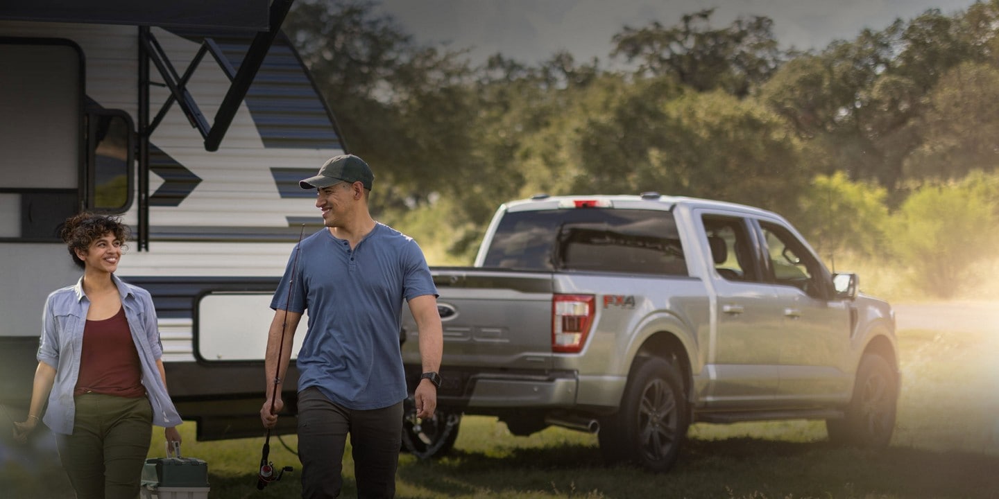 Man and woman with a dog walking near a 2023 Ford F-150® pickup hitched to a camper