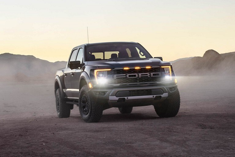 A 2023 Ford F-150® Raptor® being driven at dusk with headlights on
