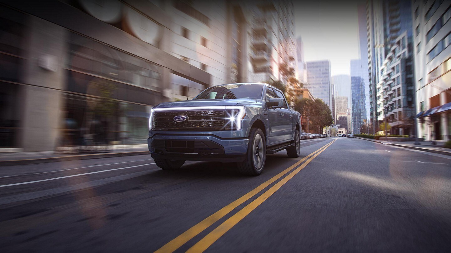 2023 Ford F-150® Lightning® in Azure Gray driving down a road in a city