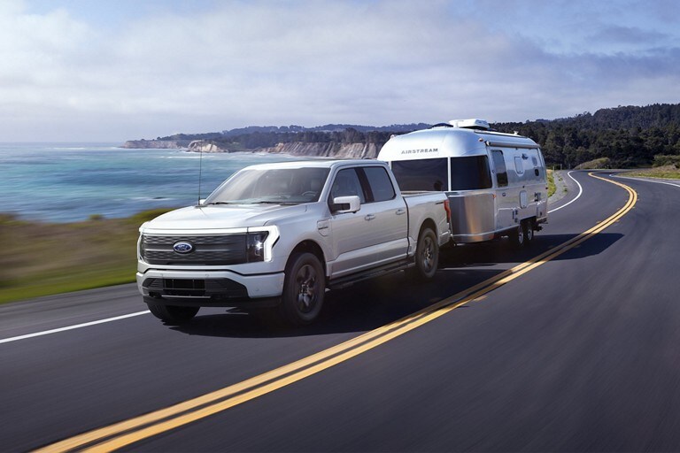 Una Ford F-150 Lightning® 2023 remolcando un tráiler para camping Airstream por un camino