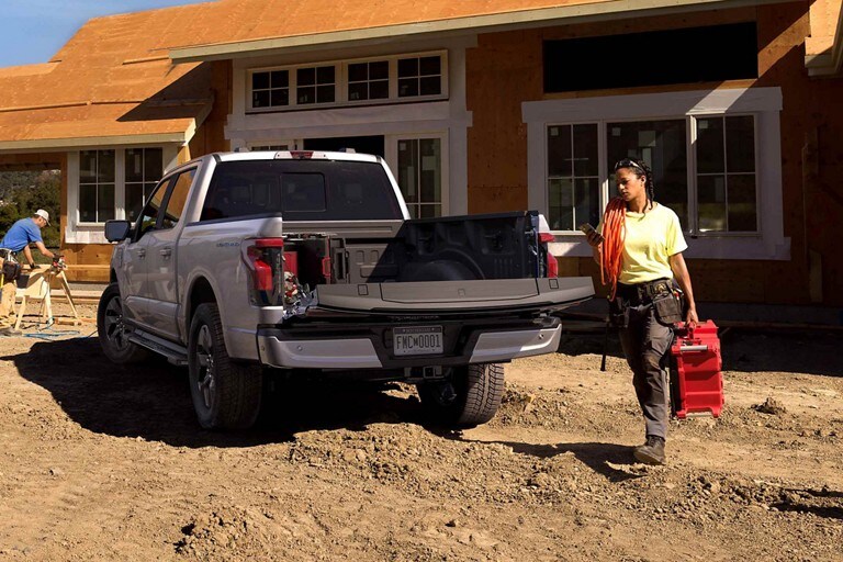 A 2023 Ford F-150 Lightning® on a construction site with the power tailgate down as a person loads up the bed with tools