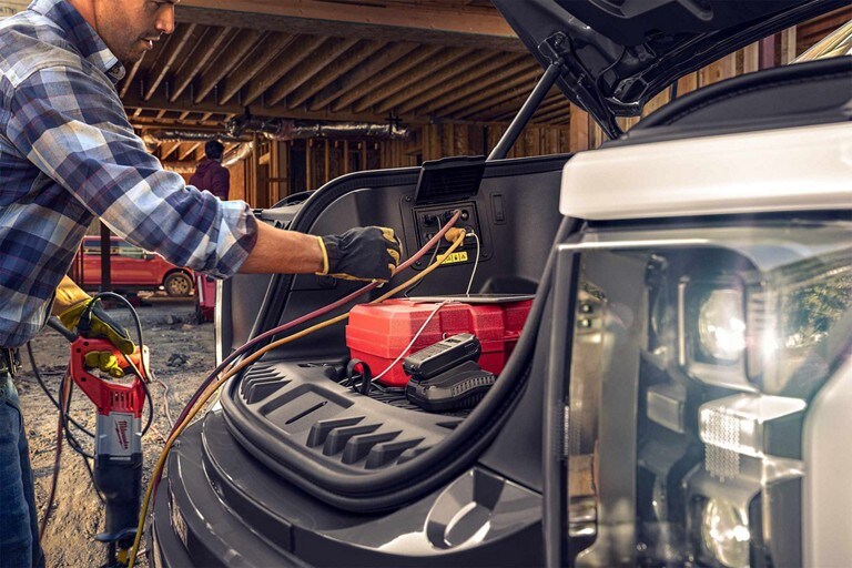 A 2023 Ford F-150 Lightning® on a house construction site showing the Mega power frunk storing items and powering tools