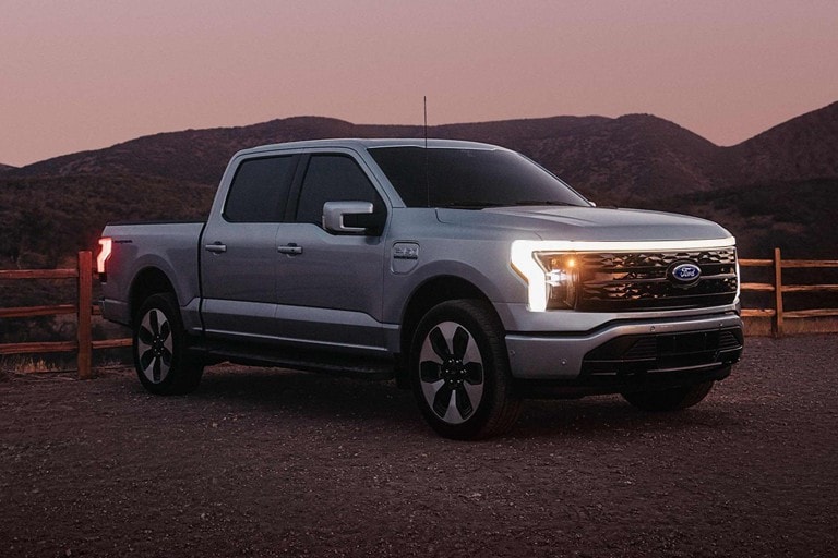 Una Ford F-150 Lightning® 2023 en un rancho al atardecer con las exclusivas luces delanteras encendidas