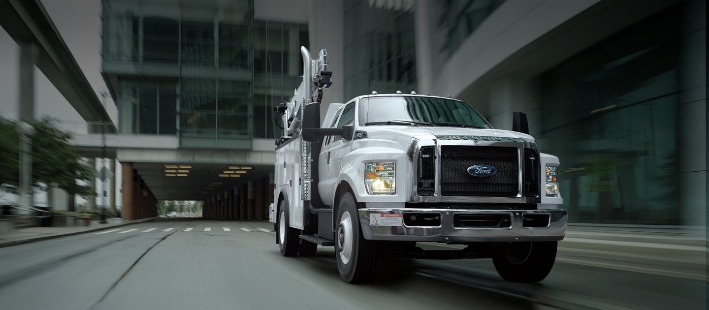 2023 Ford F-750 SuperCab with mechanic truck upfit in Oxford White being driven near large buildings