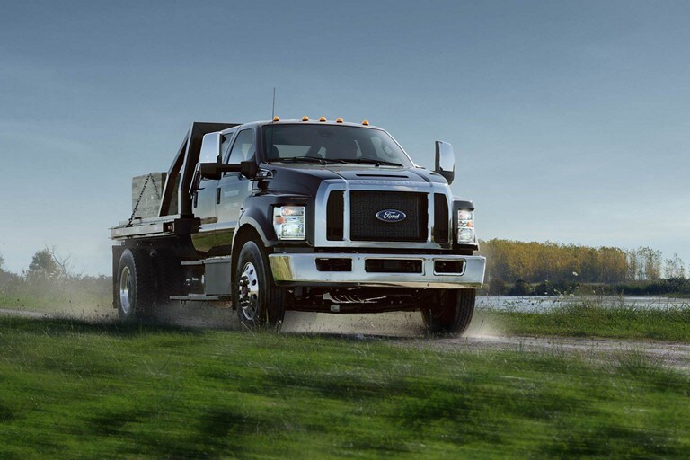 2024 Ford F-750 Crew Cab in Agate Black with utility stake bed upfit being driven on dirt path near water