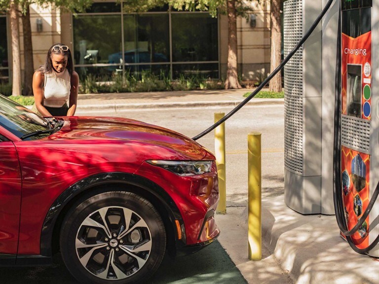 Woman at a public charging station charging a Red 2023 Ford Mustang Mach-E