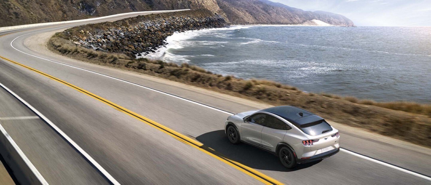 Una Ford Mustang Mach-E 2023 en Silver circulando por la carretera junto al océano