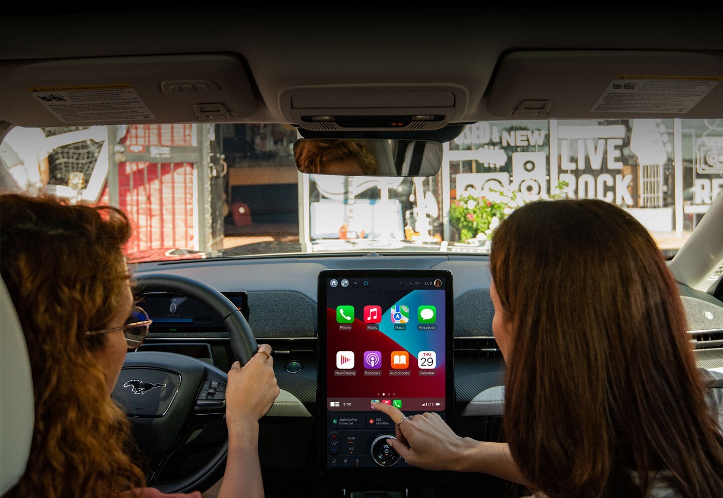 Interior de la SUV Mustang Mach-E® 2023 con una mujer conduciendo y un pasajero usando la pantalla táctil en modo retrato