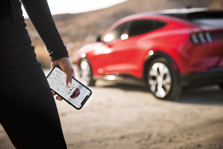 Person holding a mobile phone with a 2023 Ford Mustang Mach-E® behind them