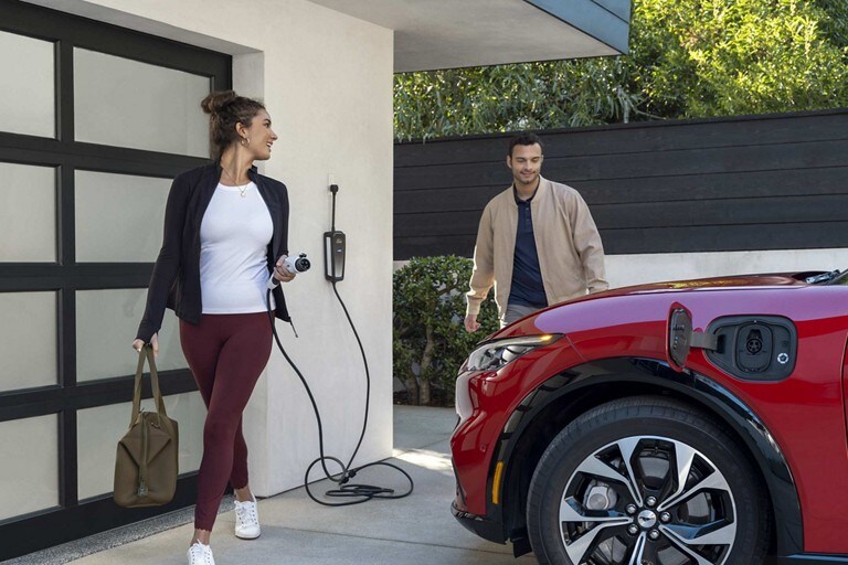 Una mujer sosteniendo un Cable de Alimentación Móvil Ford mira hacia atrás a un hombre que está mirado una Ford Mustang Mach-E® 2023