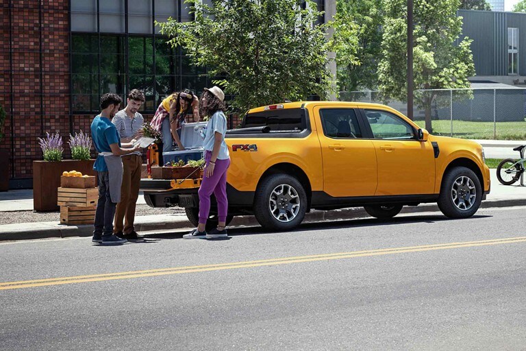 A group of friends are unloading plants from the bed of a 2023 Ford Maverick® while two men glance down at a tablet