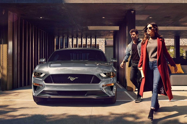 Un Ford Mustang® 2023 cupé en Carbonized Gray Metallic estacionado en un garaje con dos personas alejándose