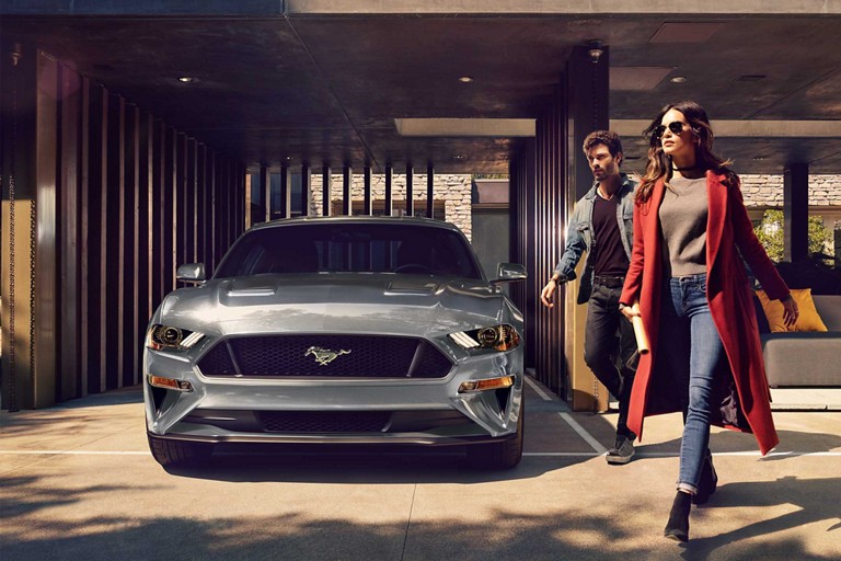 2023 Ford Mustang® coupe in Carbonized Gray Metallic parked in a carport with two people walking away