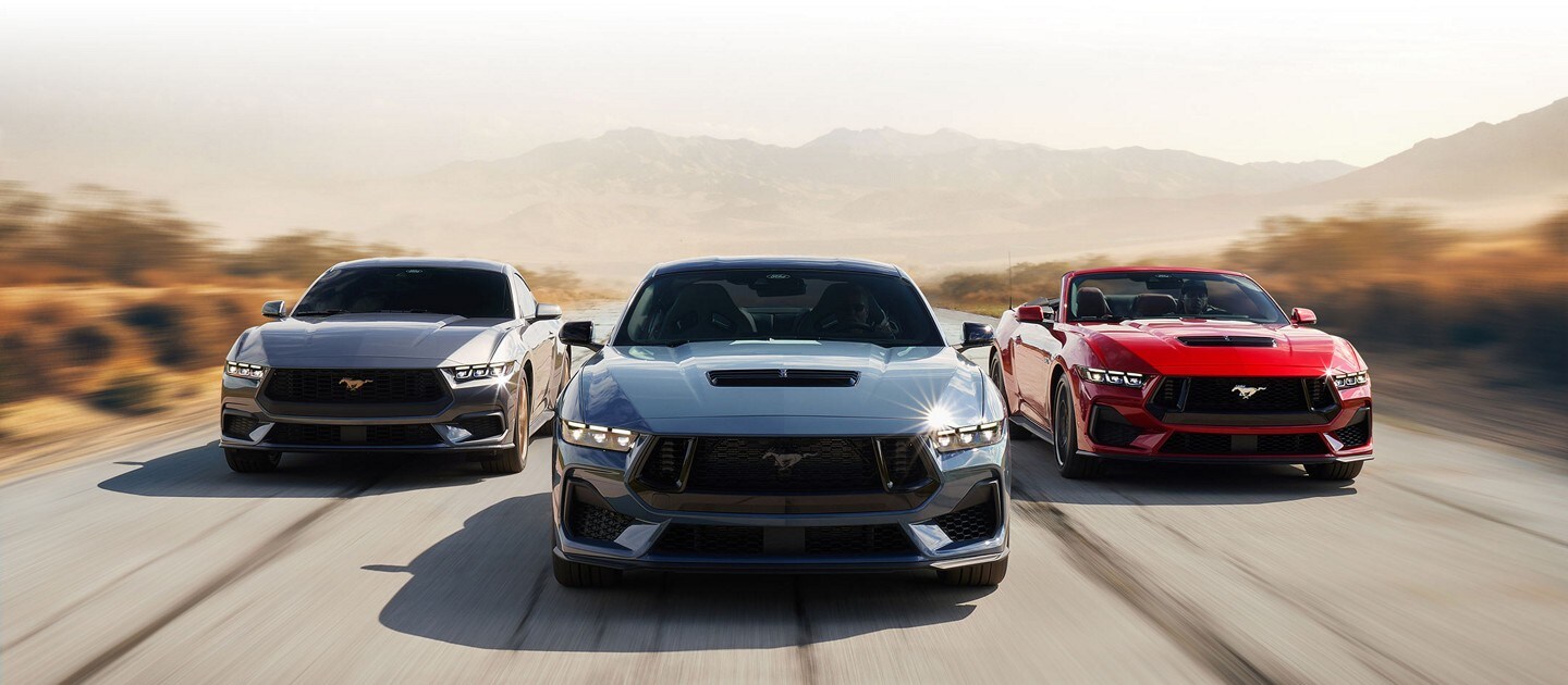 Tres modelos de Ford Mustang® 2024, dos aerodinámicos y uno convertible, andando por una carretera desértica