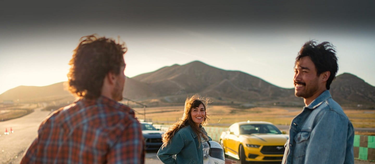 Two 2024 Ford Mustang® models parked near a racecourse with three people nearby