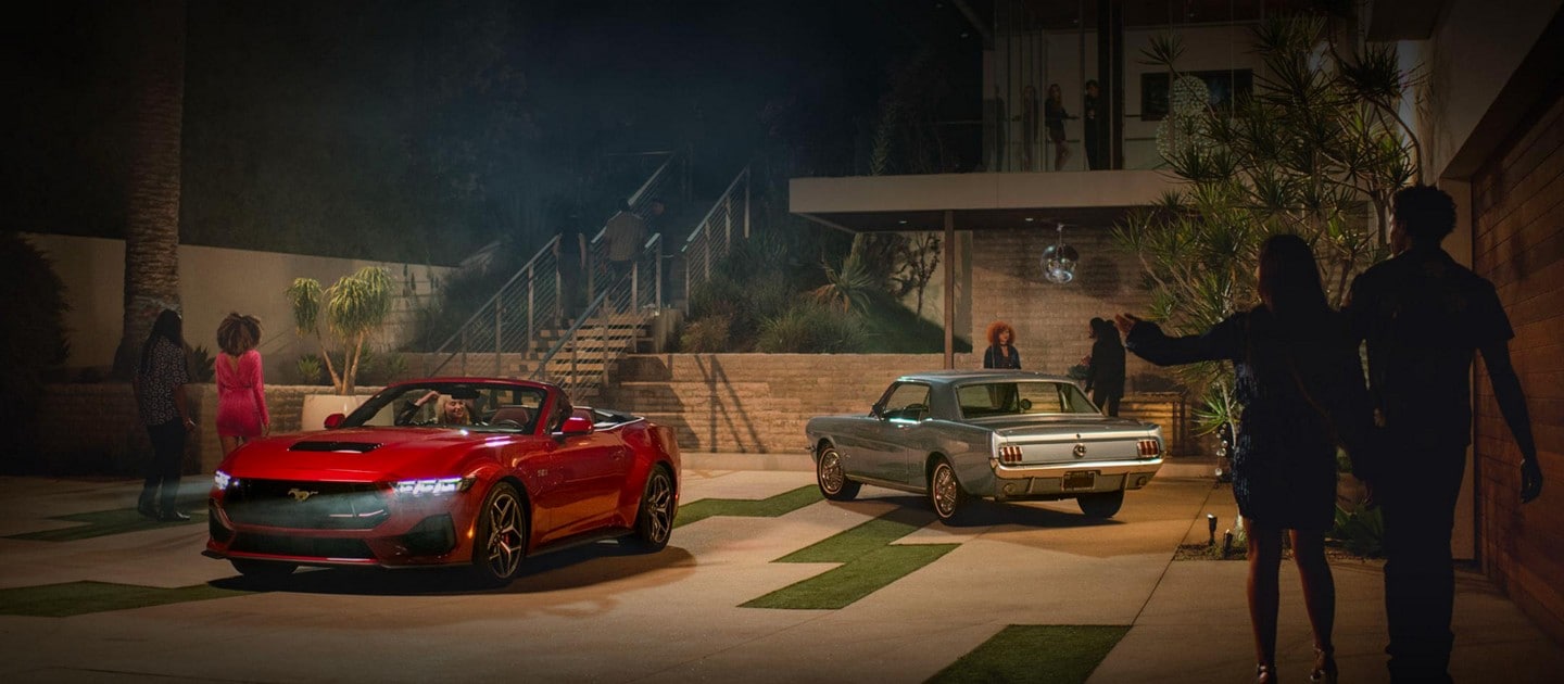 2024 Ford Mustang® GT convertible model and a first-gen Mustang model parked in a driveway with people nearby