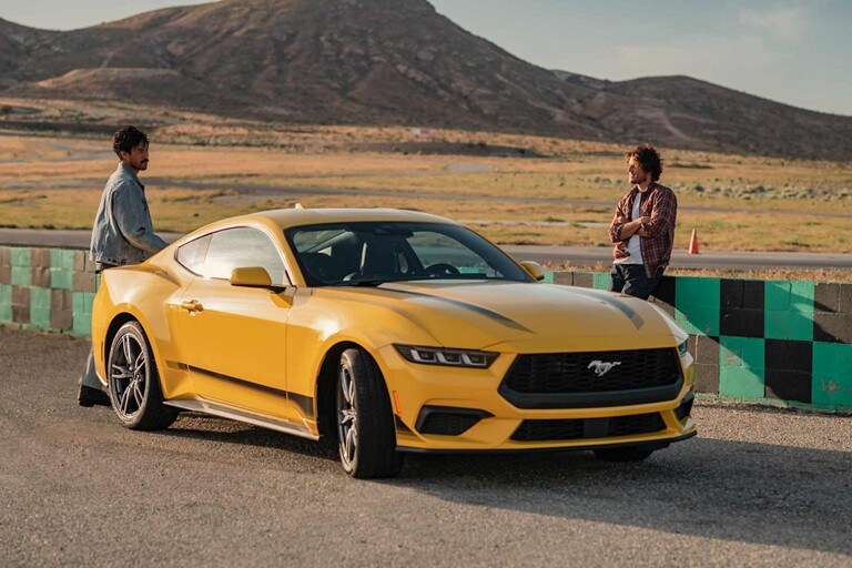 2024 Ford Mustang® EcoBoost® coupe with available Wheel and Stripe package parked on a racecourse near two people