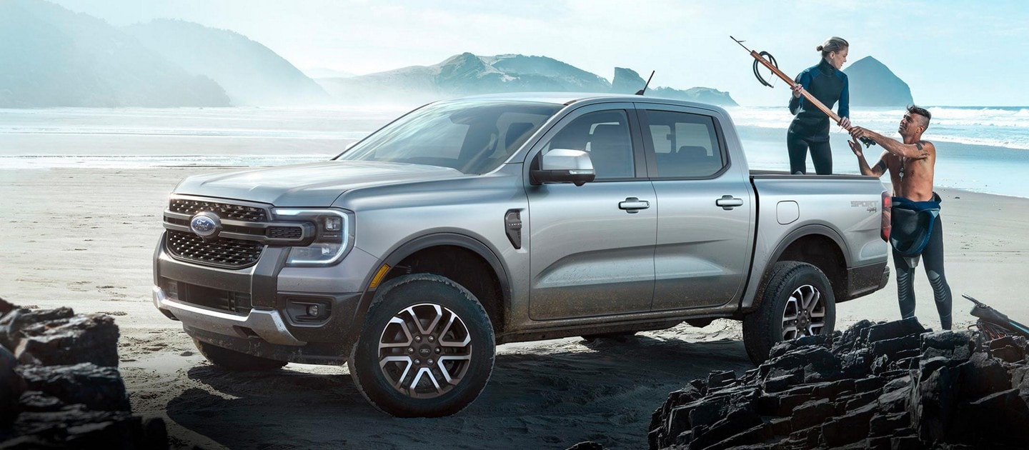 A 2024 Ford Ranger® in Azure Gray Metallic is parked at a beach location with two people unloading gear