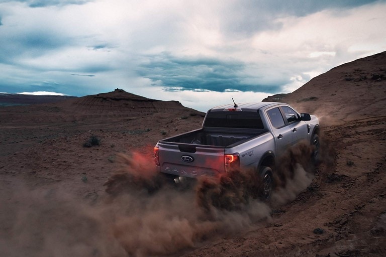 A 2024 Ford Ranger® XLT truck in Iconic Silver is being driven up a sandy dune at dusk