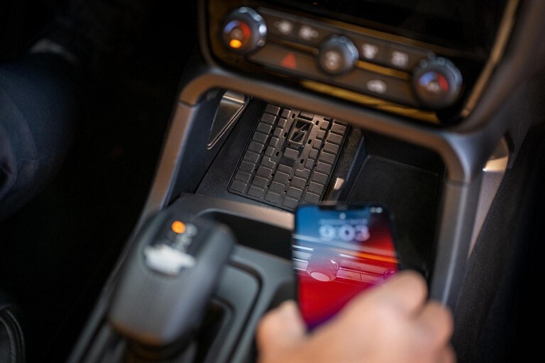 A hand placing a cell phone on the wireless charging pad in a 2024 Ford Ranger®