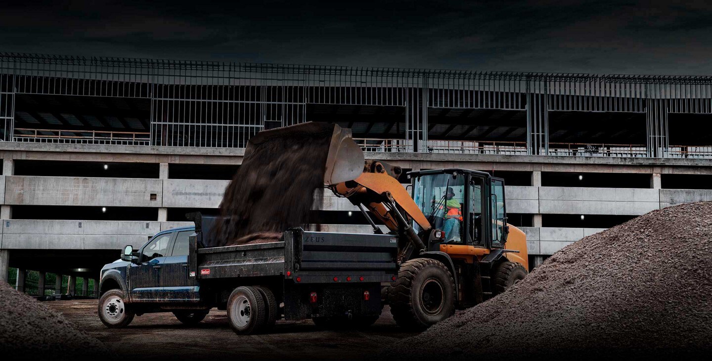 Image of a backhoe dumping dirt into the bed of a 2023 Ford Super Duty® F-600®