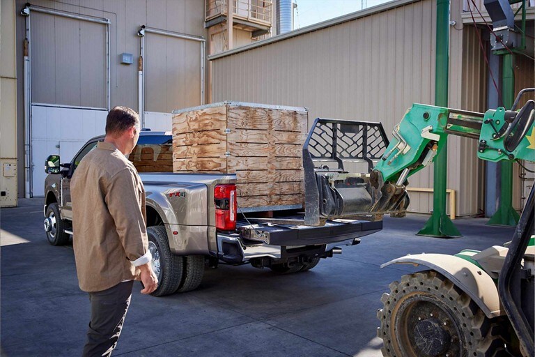 Man watching a forklift load a large crate into the bed of a 2024 Ford Super Duty® pickup