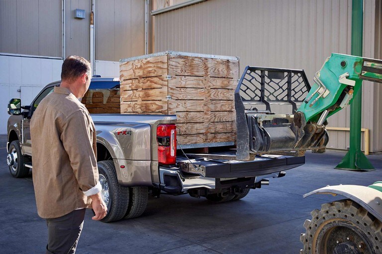 Un hombre observa cómo un montacargas carga una caja grande en la caja de una camioneta Ford Super Duty® 2023