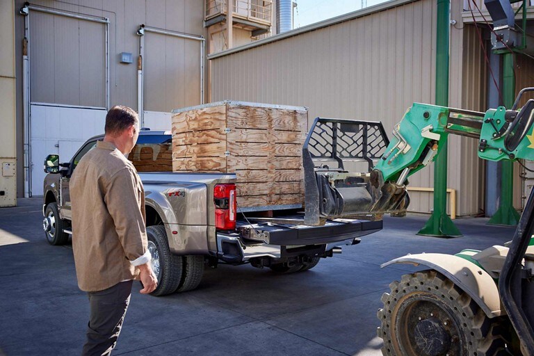 A man watching a forklift load a large crate into the bed of a 2024 Ford Super Duty® pickup