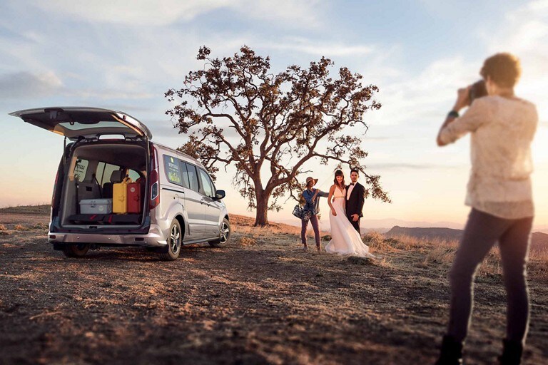 A photographer takes a photo of a bride and groom next to a 2023 Ford Transit