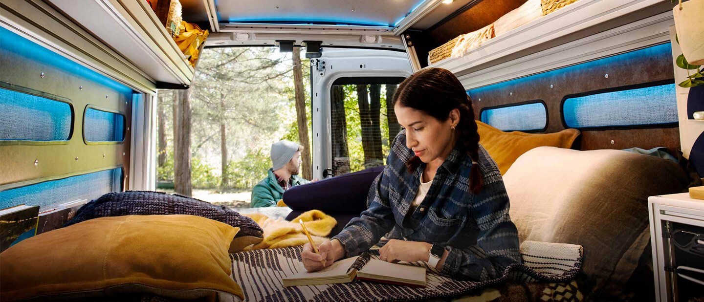 Una mujer en la parte trasera de una Transit Trail™ Van 2023 equipada para acampar