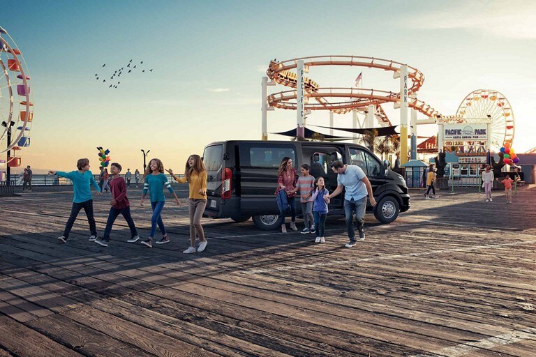 Imagen de una familia reunida alrededor de una van Ford Transit® 2023 con la puerta deslizable abierta en un parque de diversiones