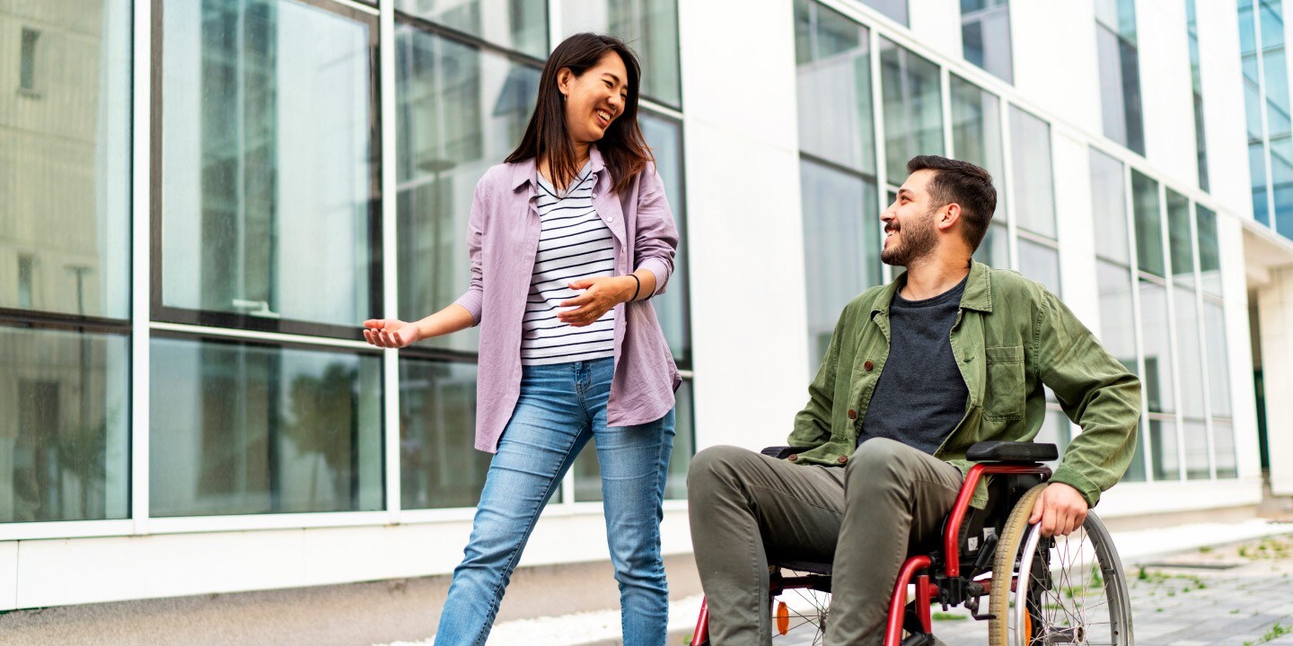 Woman walking alongside man in wheelchair while talking