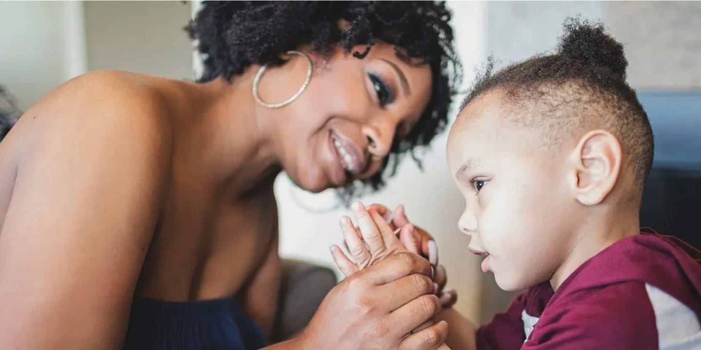 A mother holding the hands of her unsighted child, playing a clapping game