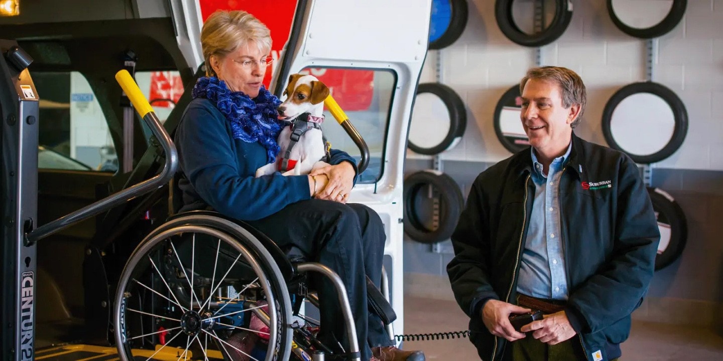 Woman holding a dog in a wheelchair inside an adapted Ford Transit van from the perspective of the back door