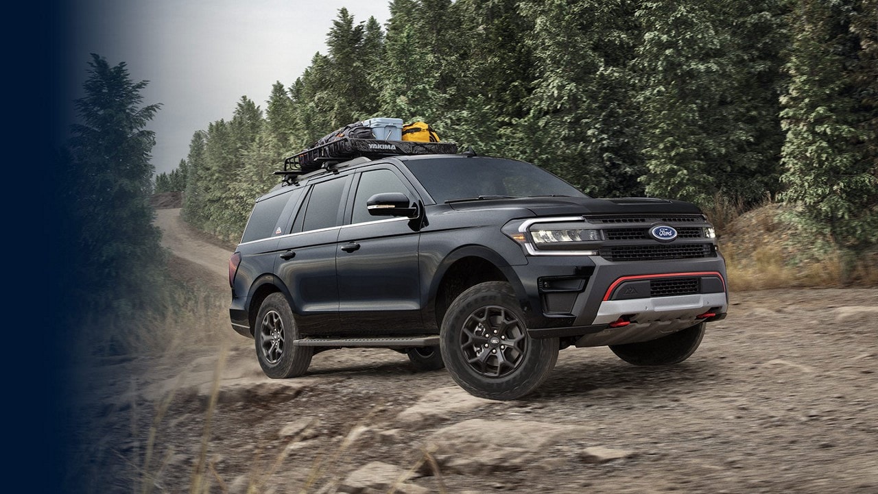 2024 Ford Expedition® being driven on a dirt road with camping gear in the roof rack